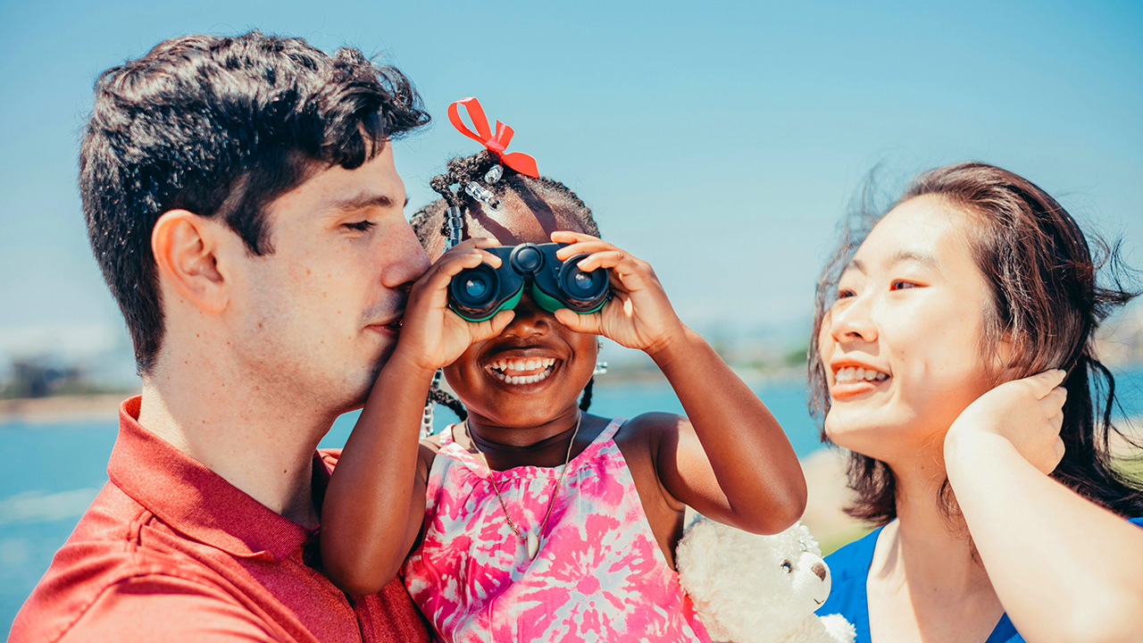 Parents holding girl who is looking through binoculars