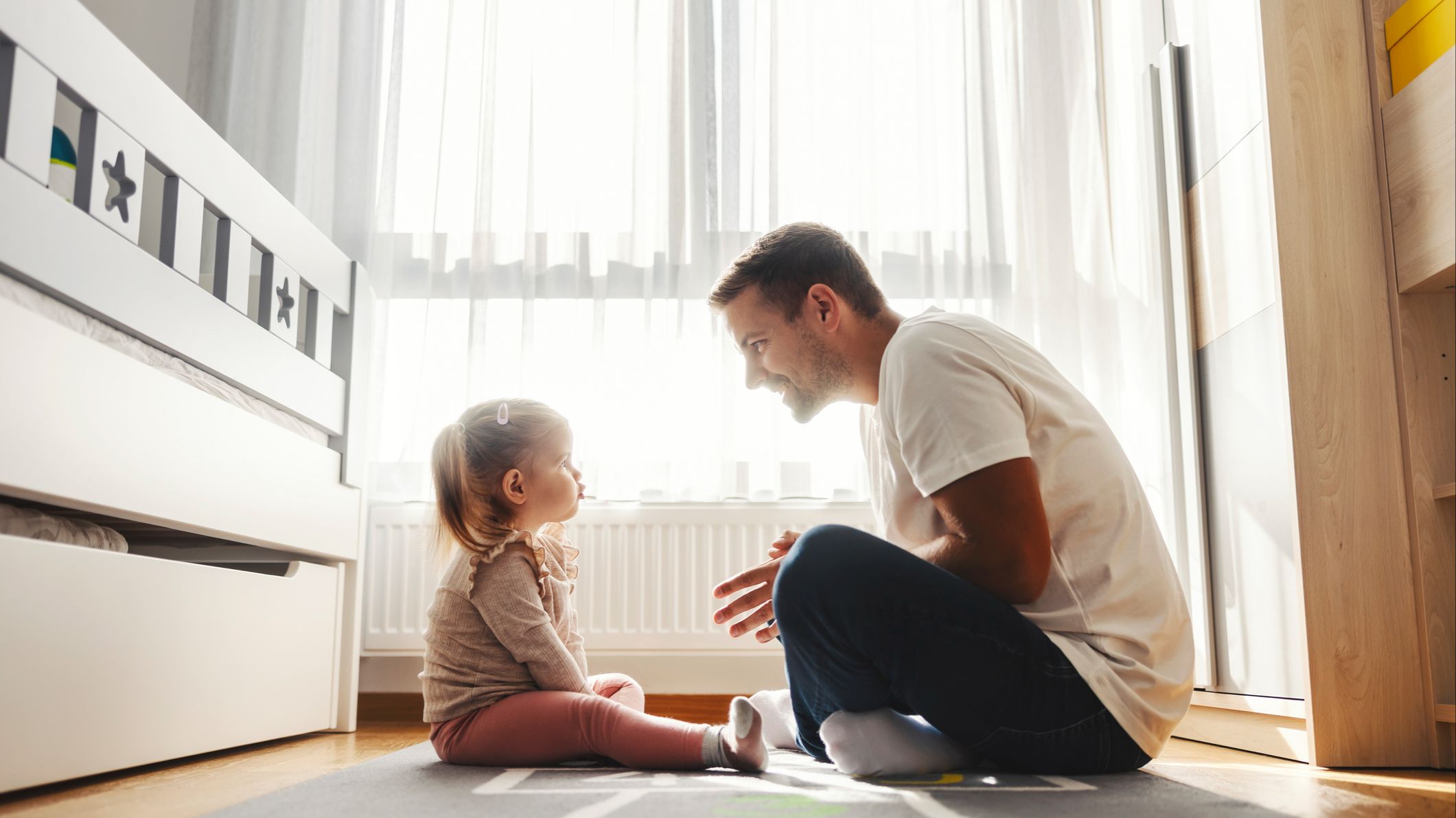 Father and daughter talking while sitting on a bedroom floor