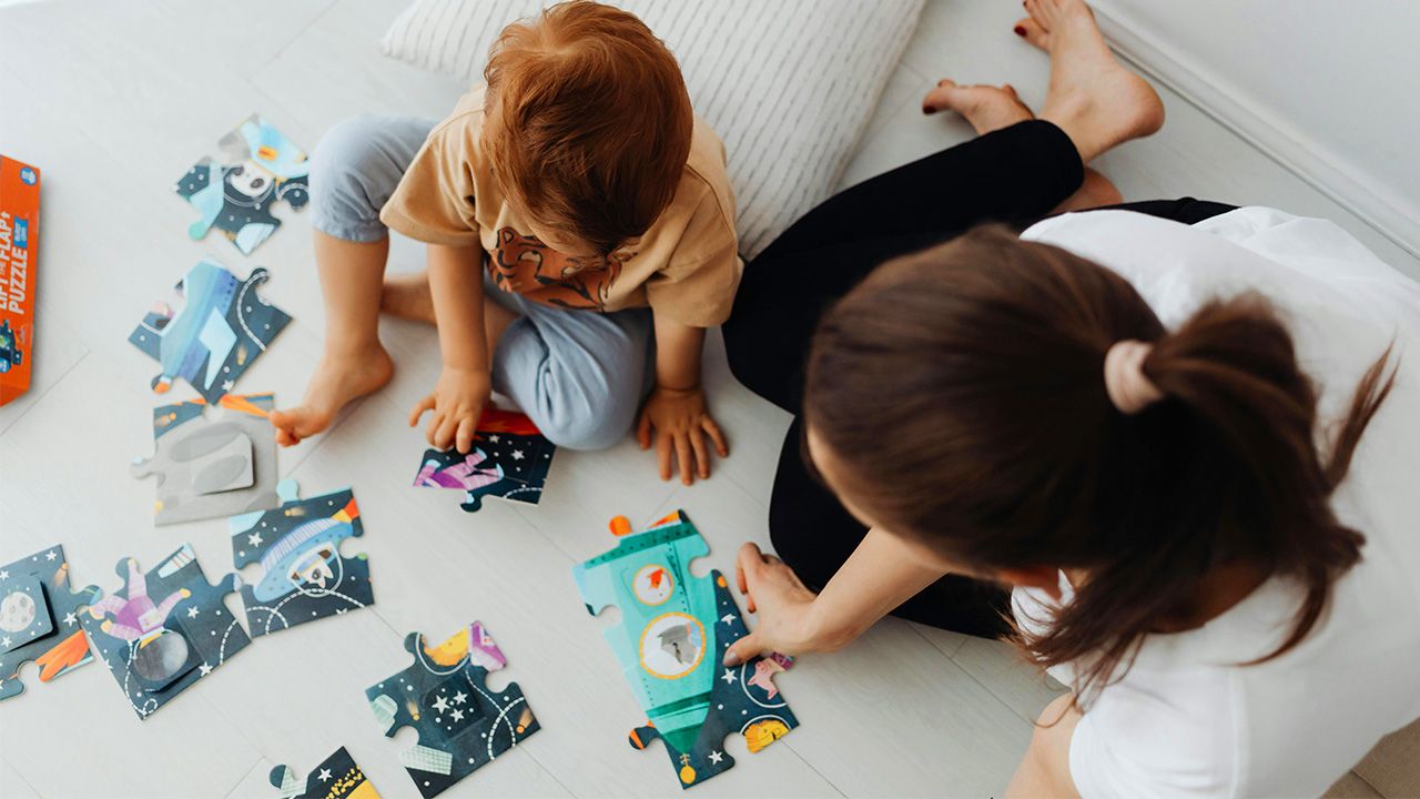 Parent and toddler sitting on the ground putting a jigsaw puzzle together