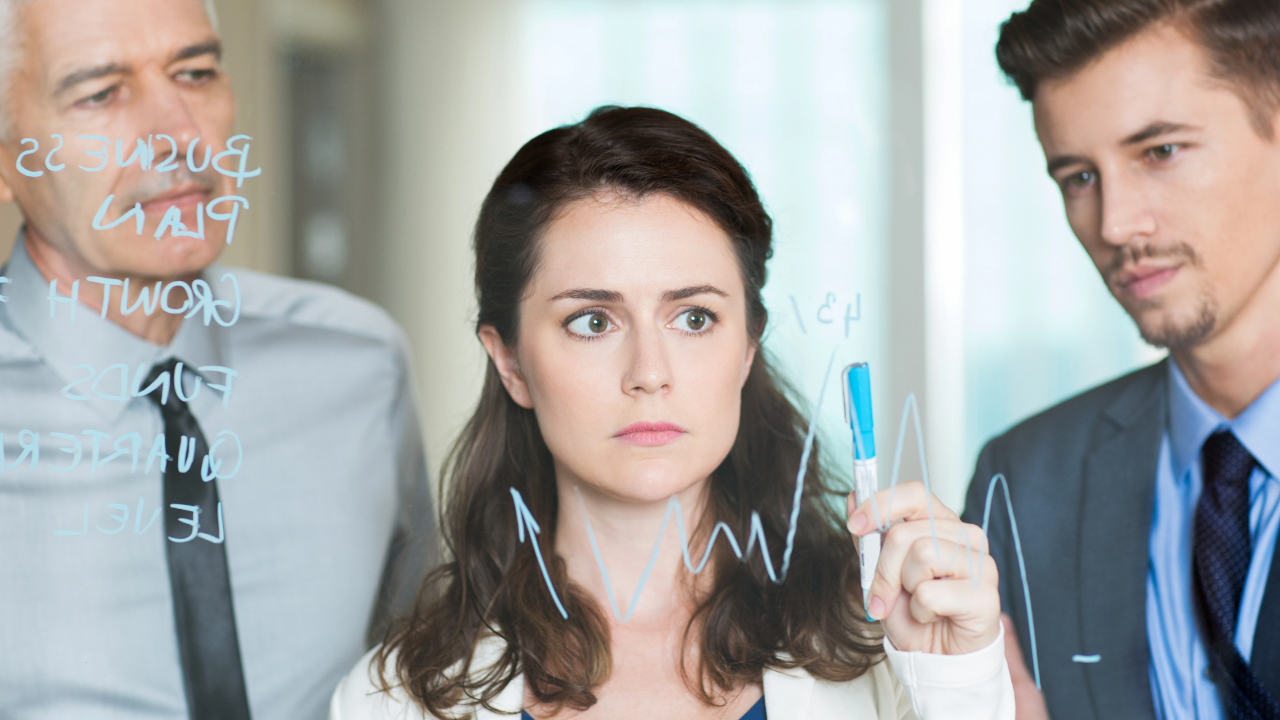 Business team analysing growth strategy with woman drawing performance chart on transparent board during meeting.