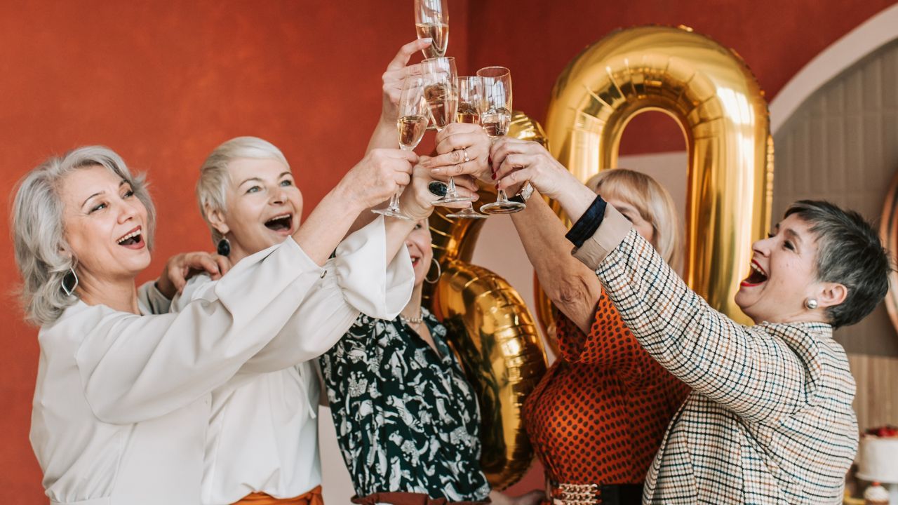 A group of midlife women raising champagne glasses in celebration, smiling and laughing together during a joyful gathering that reflects friendship, encouragement, and community.