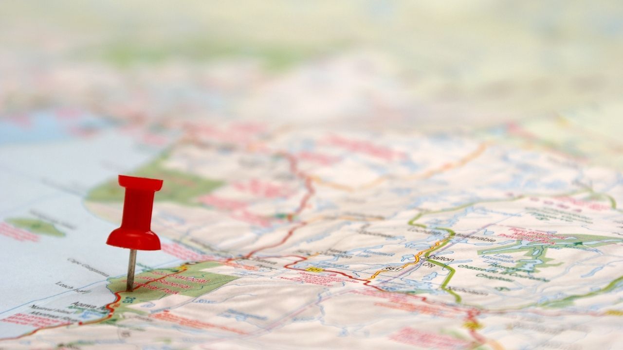 Close-up of a paper map with a red pushpin marking a location, symbolizing a change in direction and navigating an unexpected path in midlife.