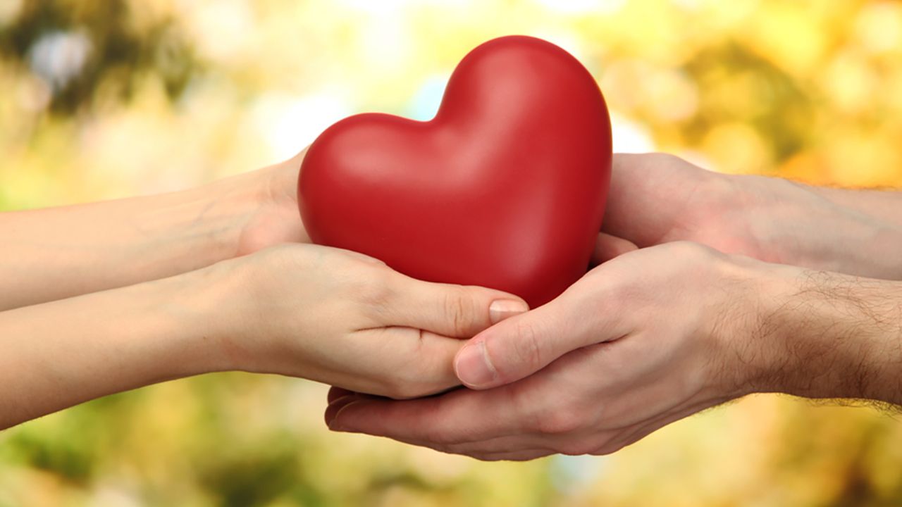 Hands gently holding a red heart symbolizing love, faith, and a peaceful connection with God.