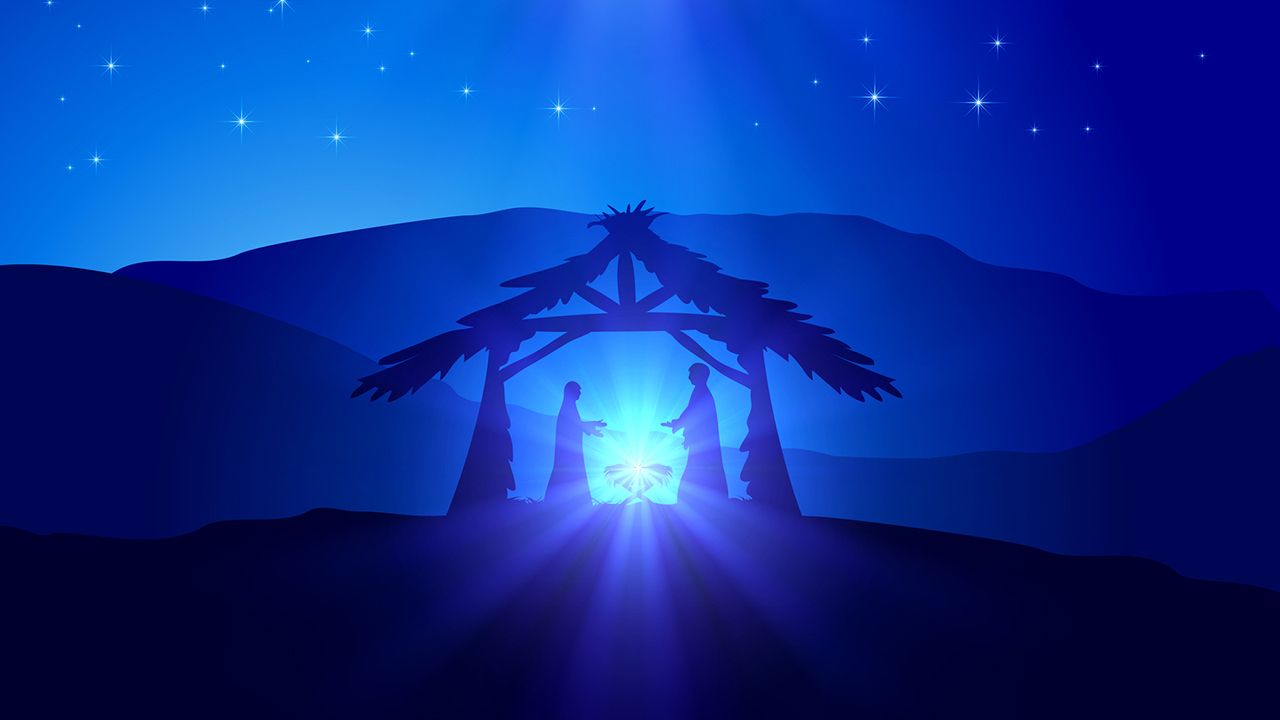 Blue illustration of the Nativity with Mary and Joseph standing beside baby Jesus in a manger under a simple wooden stable, with bright light shining from the child and stars in the night sky.