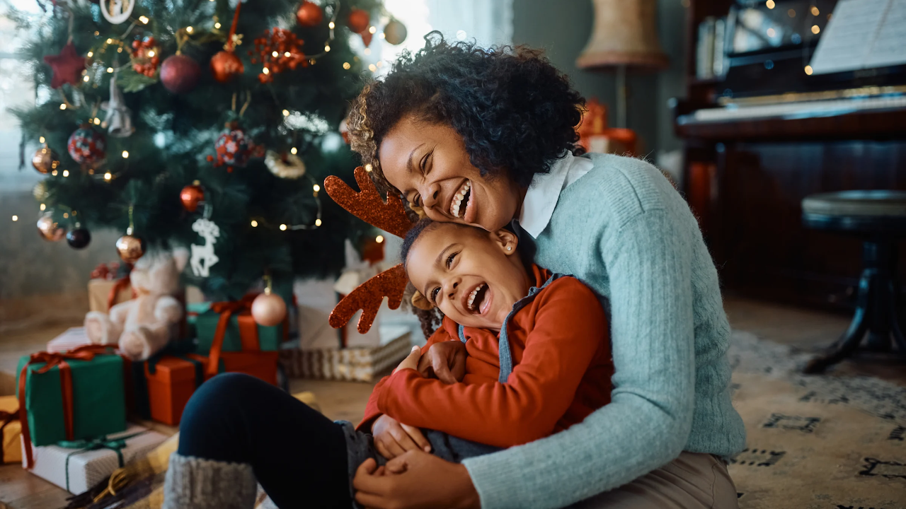 Parent and child sharing a quiet holiday hug in a softly lit room decorated for Christmas, capturing warmth and emotional connection