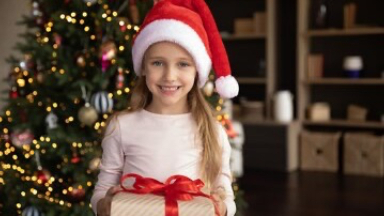 A young child holding a wrapped Christmas present with a joyful, excited expression.