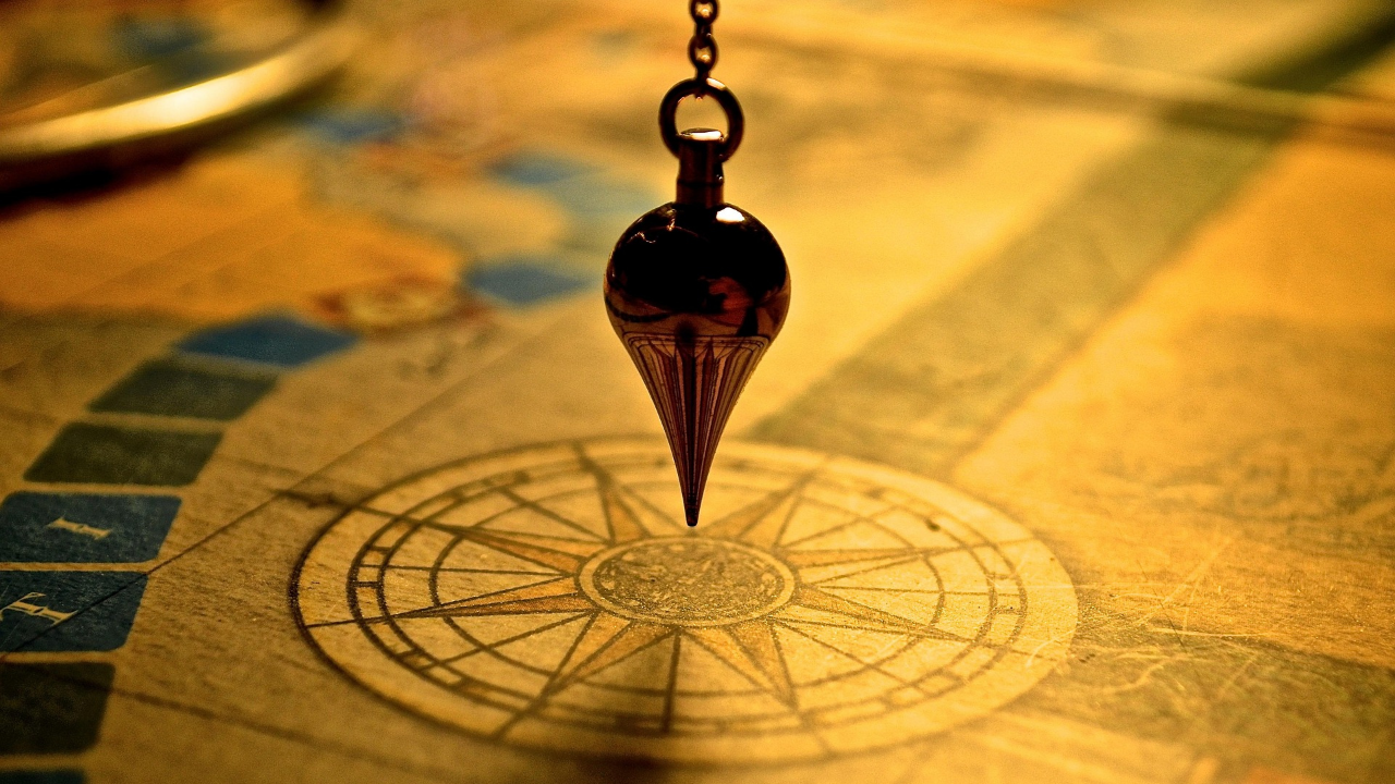 Pendulum suspended over a compass symbolizing leadership judgment and the internal signal leaders sense before making an important decision.