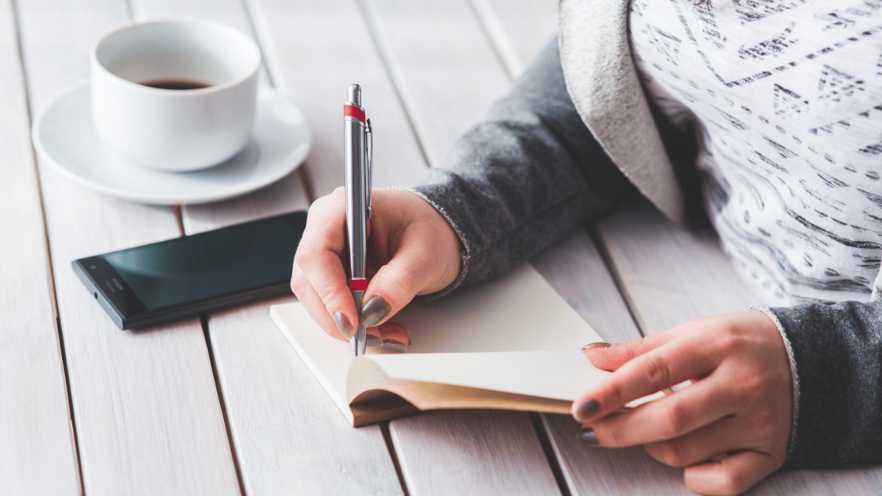 Person journaling at a desk with a cup of tea and plants, representing mindfulness, self-care, and setting healthy boundaries.