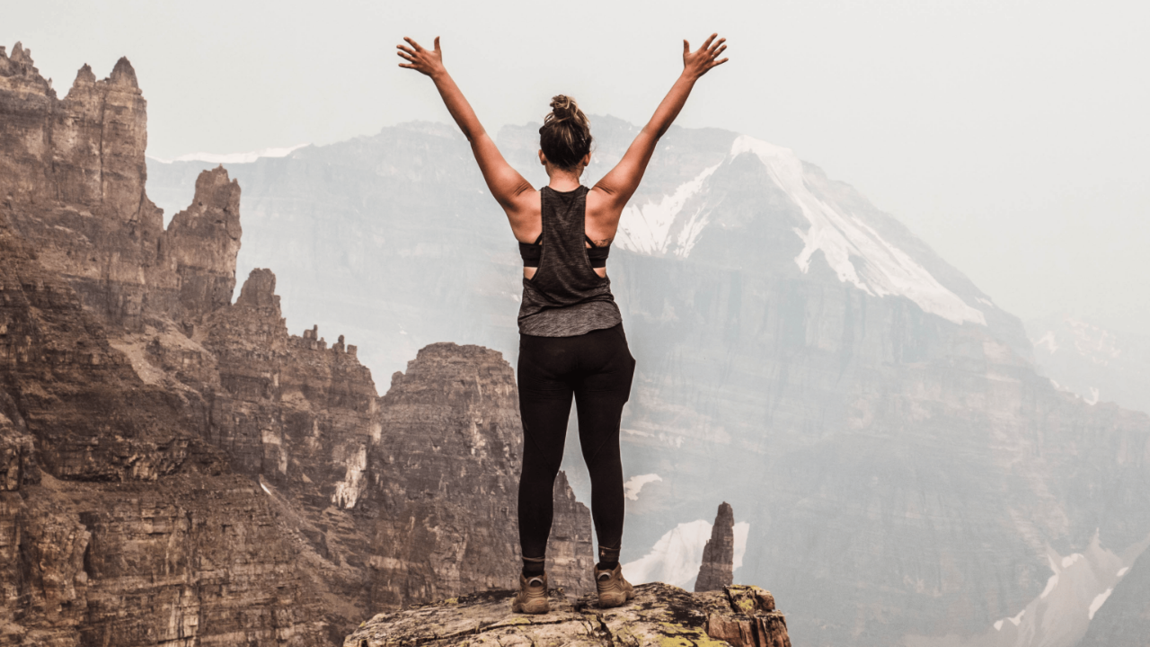 Confident person standing on a mountain peak at sunrise, symbolizing self-confidence and personal growth.