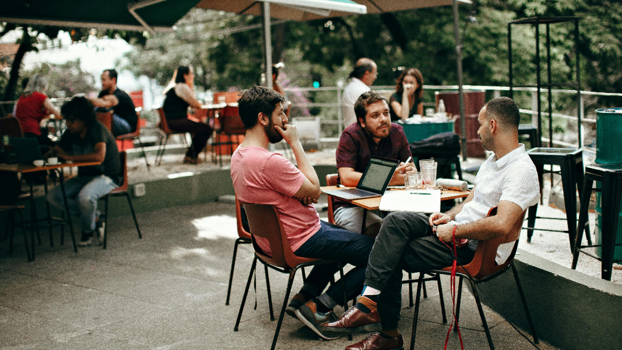 three men sitting at a table with a lap top computer having a discussion