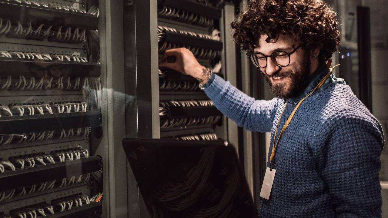 IT-Techniker überprüft Server-Rack und Netzwerkverkabelung mit Laptop in professioneller IT-Infrastruktur