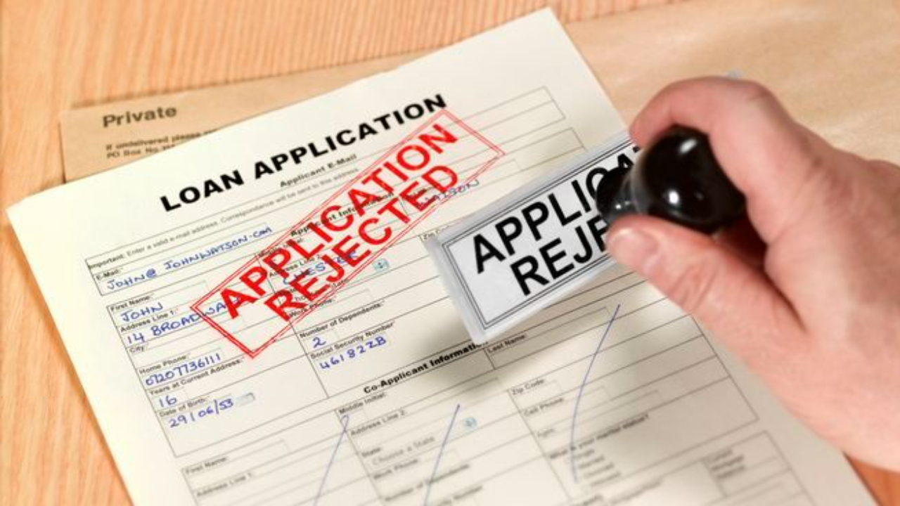 A hand stamping a loan application form with the red 'APPLICATION REJECTED' seal, symbolizing a business loan denial