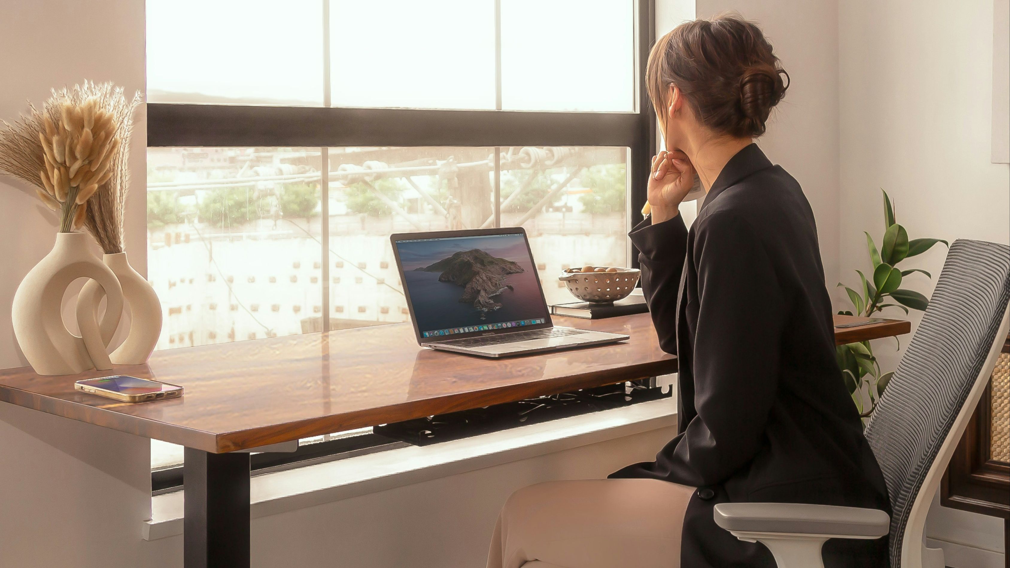 woman sitting in office chair at desk with laptop open staring out the window