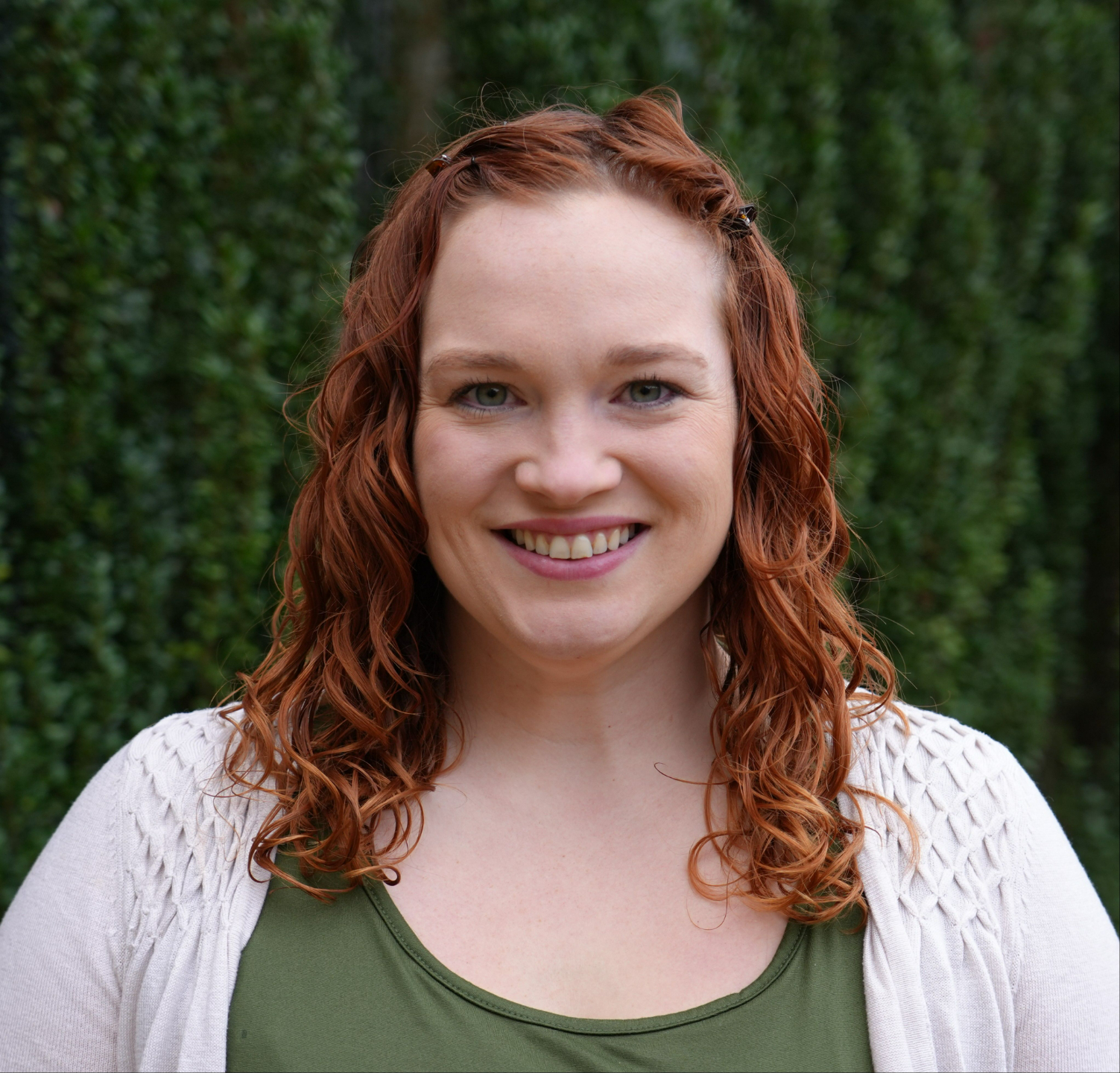 Madison Stepherson, a woman with curly red hair, smiles against a green backdrop.