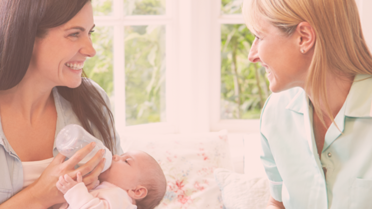 A mom feeding her baby a bottle while having a conversation with another woman
