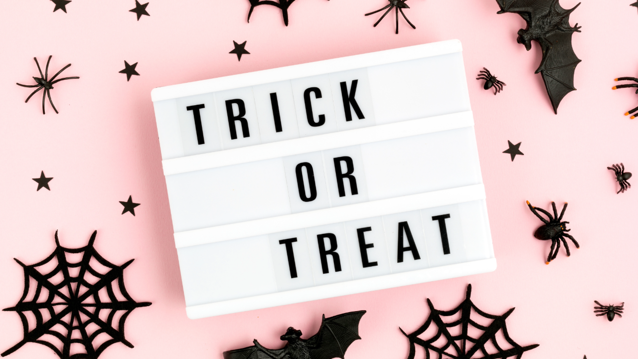Lightbox sign reading ‘Trick or Treat’ on a soft pink background, surrounded by small Halloween decorations like bats, spiders, and spiderwebs.