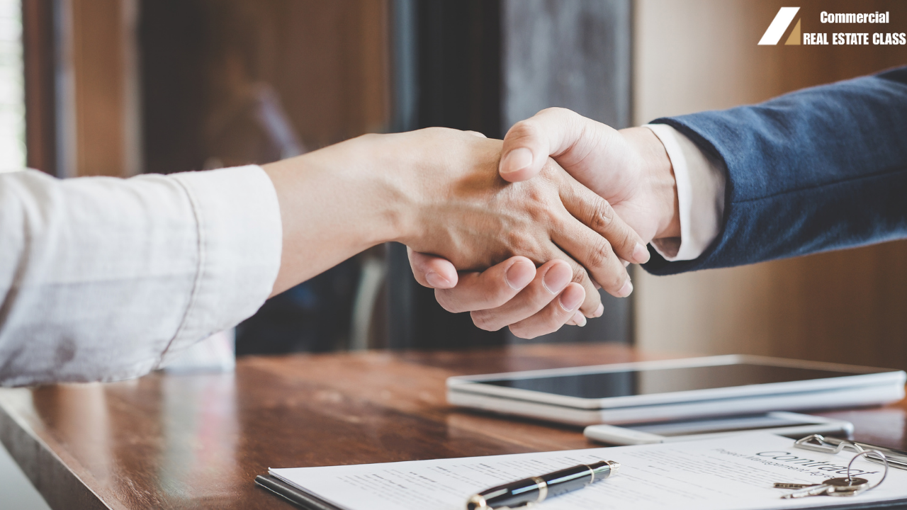 Two professionals shaking hands over a commercial lease agreement with keys and documents on a table representing a finalized real estate lease deal