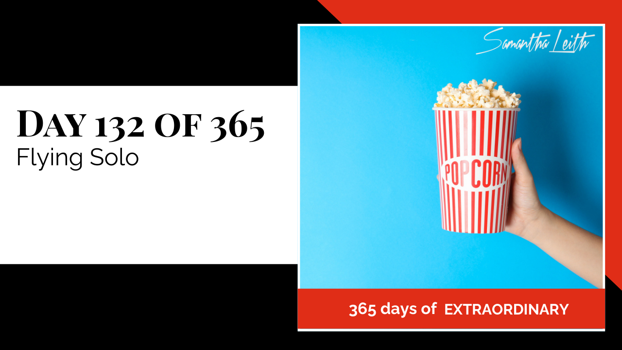 Blog image for Day 132 of Sam Leith's '365 Days of Extraordinary' series, featuring a hand holding a large, red and white striped bucket of popcorn against a bright blue background, symbolizing the movie or experience of 'Flying Solo' or embracing entertainment and independence.