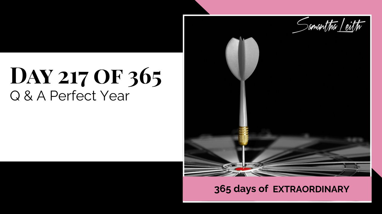 A photographic post featuring a close-up, high-contrast image of a dart hitting the center red bullseye of a dartboard. The dart has a silver flight and tip, with a gold knurled band. The dartboard is mostly grayscale with the center bullseye in red. The image is split with a title card on the left side that reads: "DAY 217 OF 365 Q & A Perfect Year". Below the photo, a magenta banner reads: "365 DAYS OF EXTRAORDINARY". A stylized signature in the top right corner says "Samantha Leith.