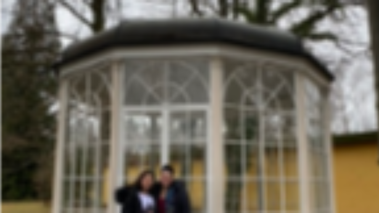 A photo of two individuals standing in front of the glass summer house (gazebo) from the movie The Sound of Music, used to illustrate a travel blog post about taking the official Sound of Music tour in Salzburg, Austria, and visiting famous film locations.