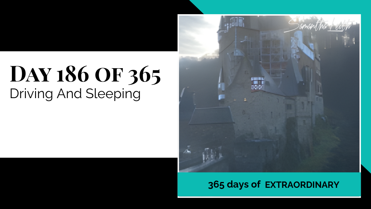 A high-contrast photograph of a medieval European castle surrounded by fog and trees, representing a travel destination and illustrating a blog post about the challenges of long-distance driving, finding lodging, and managing sleep while traveling abroad.