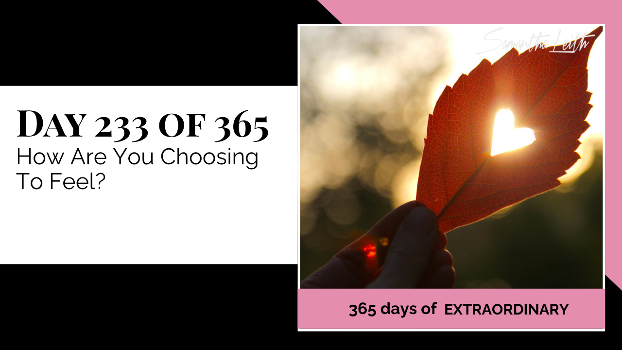A photographic post featuring a close-up of a person's hand holding a red autumn leaf up to the sun. The leaf has a heart-shaped hole cut into its center, allowing the warm, bright sunlight to shine through. The image is split with a title card on the left side that reads: "DAY 233 OF 365 How Are You Choosing To Feel?". Below the photo, a bright pink banner reads: "365 DAYS OF EXTRAORDINARY". A stylized signature in the top right corner says "Samantha Leith."