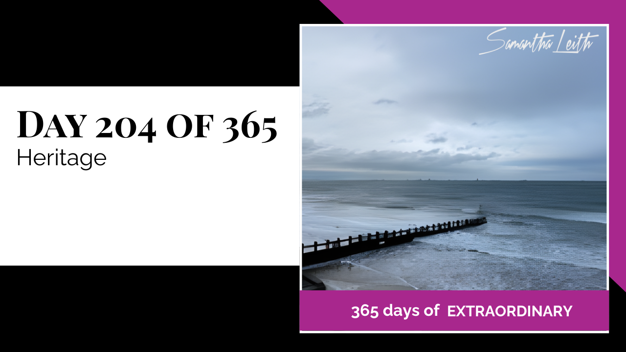 A wide-angle landscape photograph of a rugged shoreline featuring an old wooden groyne jutting into the gray sea under a heavy sky, used as a powerful visual metaphor to discuss cultural heritage, historical preservation, and personal legacy.