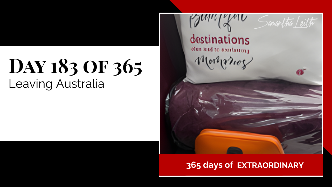 In-flight photograph of an airline seat with a dark purple blanket and a pillow labeled with travel themes like 'destinations' and 'memories', used to illustrate the experience of international travel, airport logistics, and leaving Australia for a new destination.