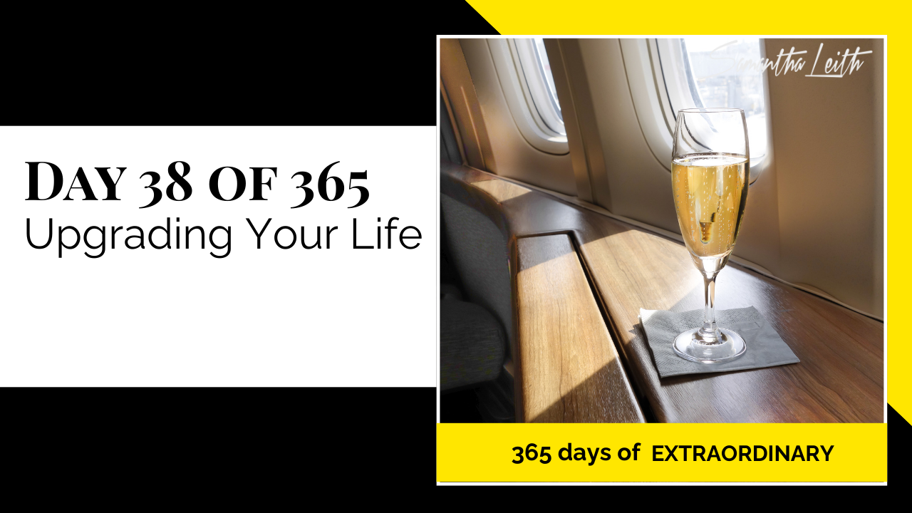 A promotional graphic for Day 38 of 365 of a series by Samantha Leith titled "365 days of EXTRAORDINARY". The text highlights the day's topic: "Upgrading Your Life". The visual on the right is a luxurious photo taken inside a first or business class airplane cabin, showing a flute of sparkling champagne resting on a polished wood table next to a sunny window. This imagery symbolizes luxury, success, aspirational goals, self-improvement, and upgrading one's lifestyle or circumstances.