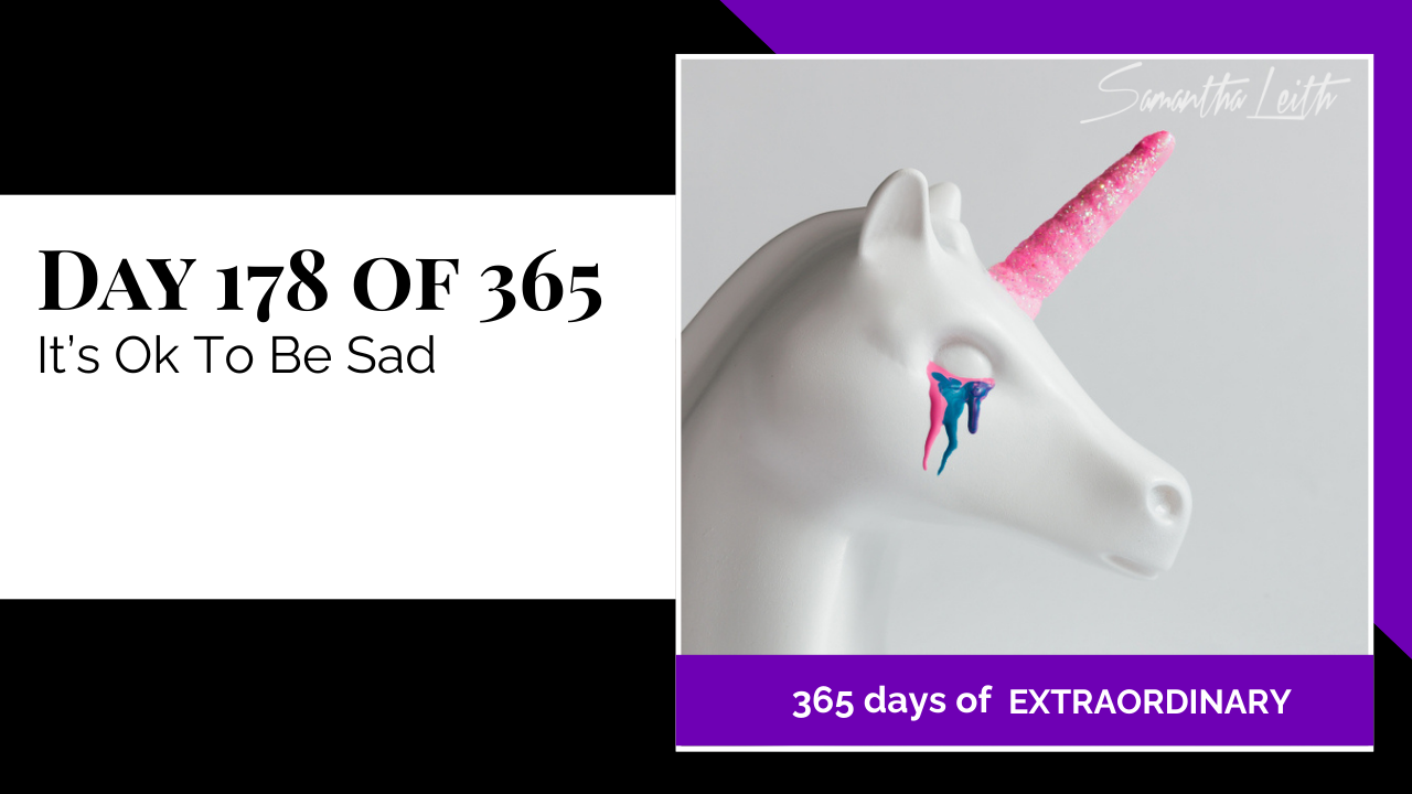 A close-up studio shot of a white unicorn statue with brightly colored tears (pink and blue) and a sparkling horn, used as a powerful, contemporary visual metaphor for mental health, emotional acceptance, and normalising sadness.