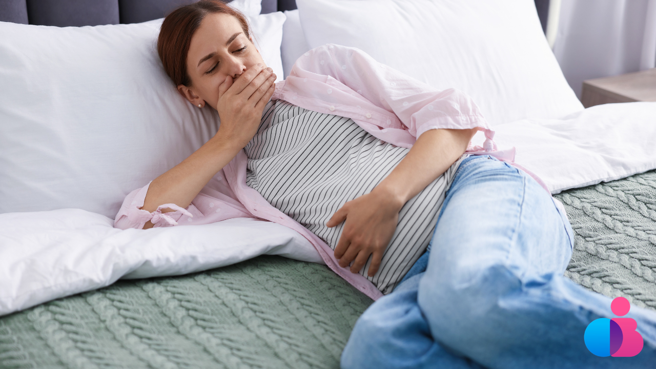 Pregnant woman laying on bed holding her belly with one hand and covering her mouth with the other hand