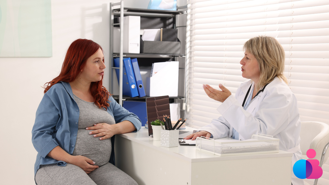 Pregnant woman and doctor discuss questions across a desk.