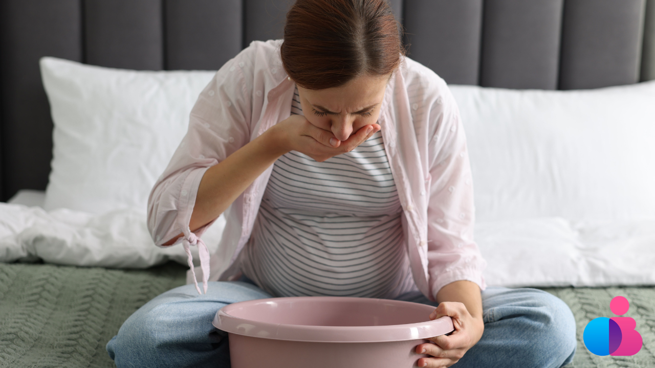 Pregnant woman sitting on a bed cupping her mouth and bending over a bowl