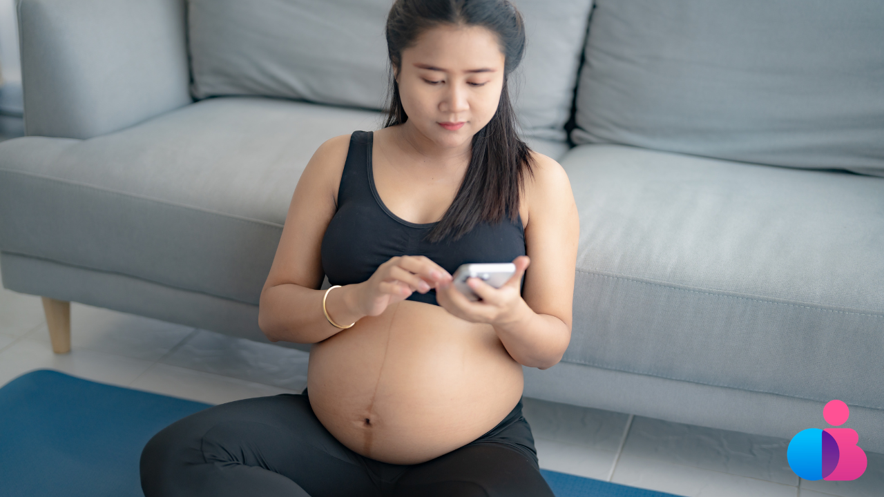 Pregnant woman researching pregnancy symptoms on her phone at home.