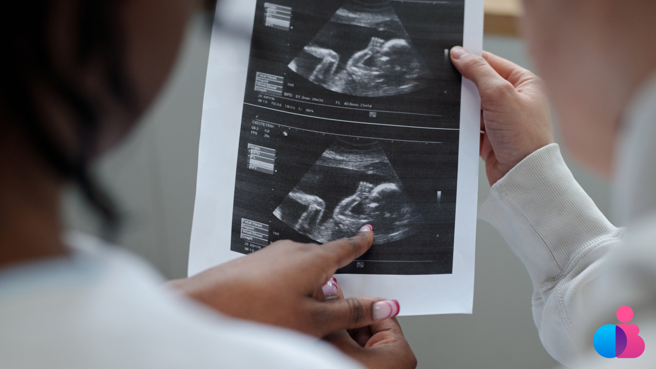 Doctor and patient looking at a printed ultrasound image of the patient's pregnancy, both people have a hand on the image and the patient is pointing to her baby's face