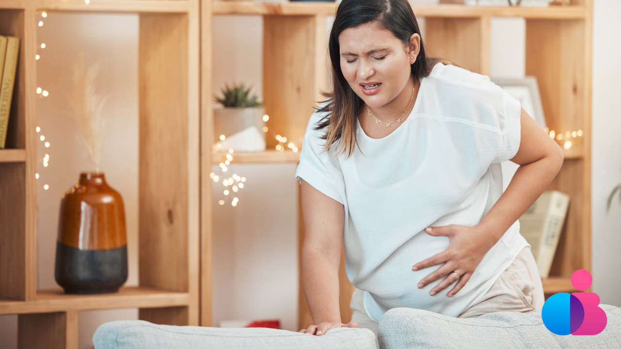 Pregnant woman holding her belly and leaning forward with a pained expression.
