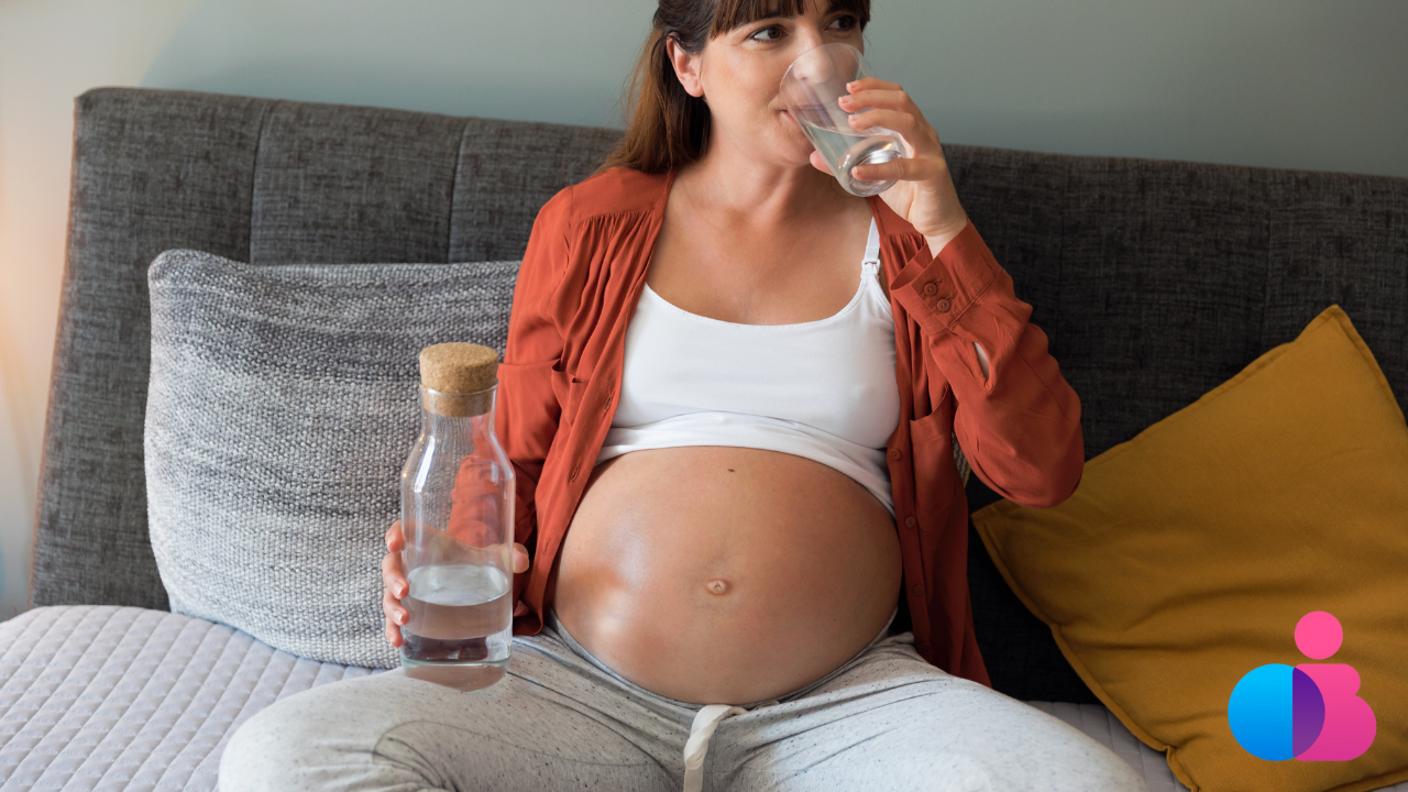 pregnant woman sitting on a couch drinking a glass of water