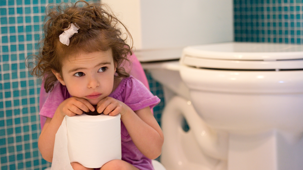 Toddler sat holding toilet paper next to the toilet