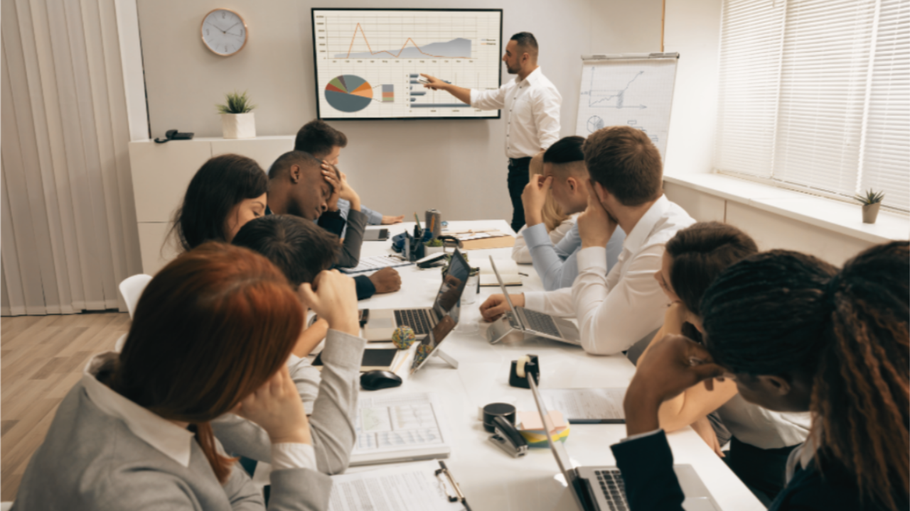 Executive Business Man conducting a training and the people around the boardroom table are bored - Corporate Gems