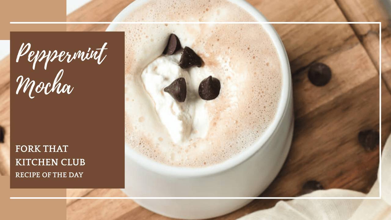White mug of peppermint mocha topped with whipped cream and dark chocolate chips on a wood cutting board with a few chocolate chips sprinkled around the mug and an ivory colored linen napkin to the side