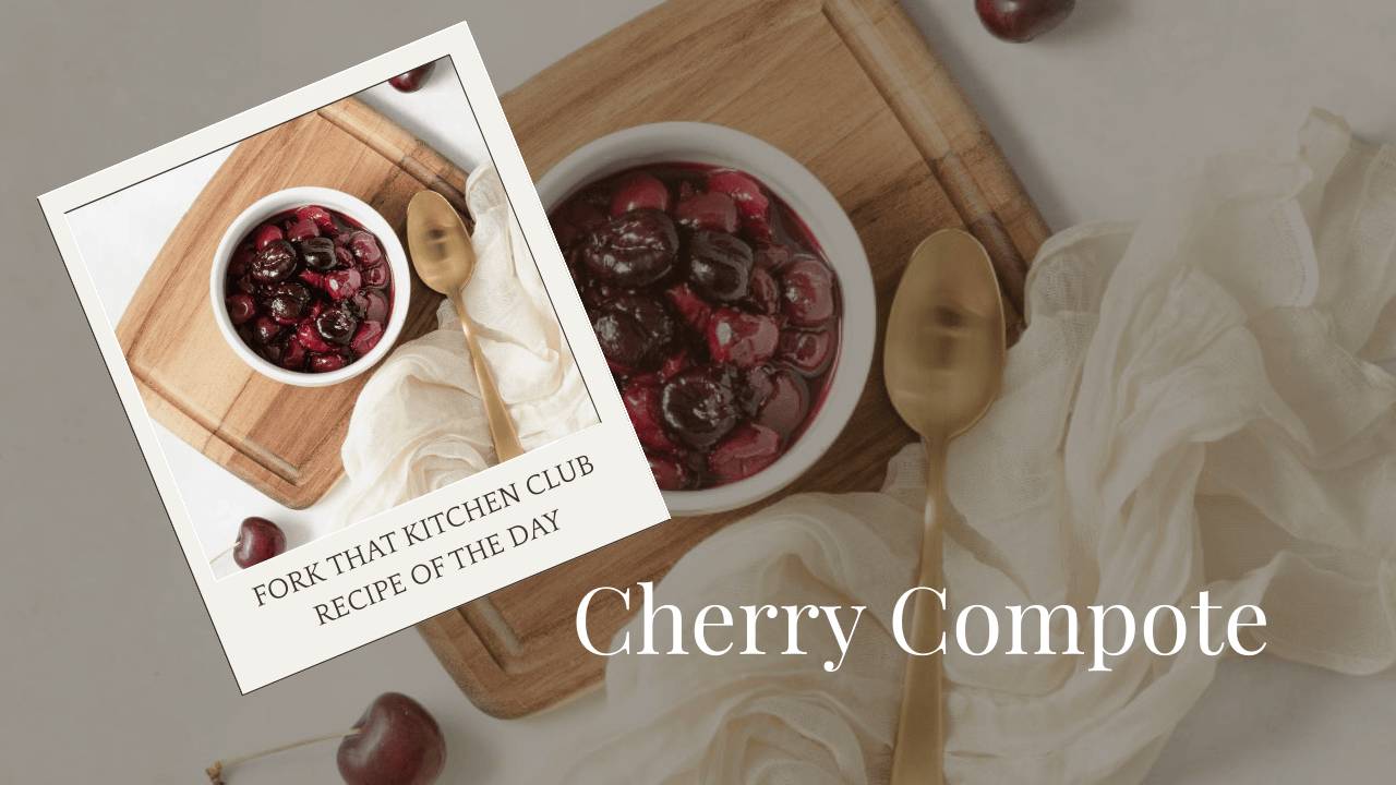 White bowl of ruby-red cherry compote on light wooden surface with gold spoon beside it, off-white linen napkin underneath, scattered fresh cherries in background