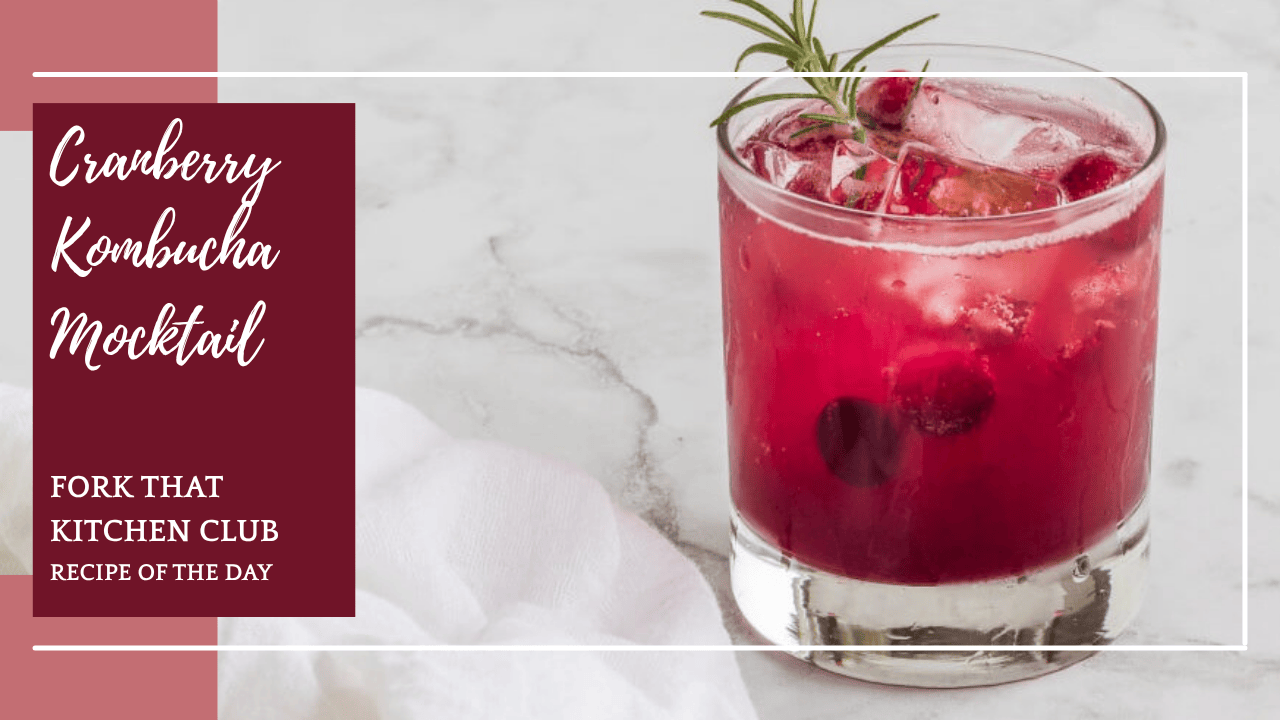 Glass of Cranberry Kombucha Mocktail with sparkling water, frozen cranberries, and fresh rosemary garnish served over ice on a white & gray marble surface and a white linen napkin nearby