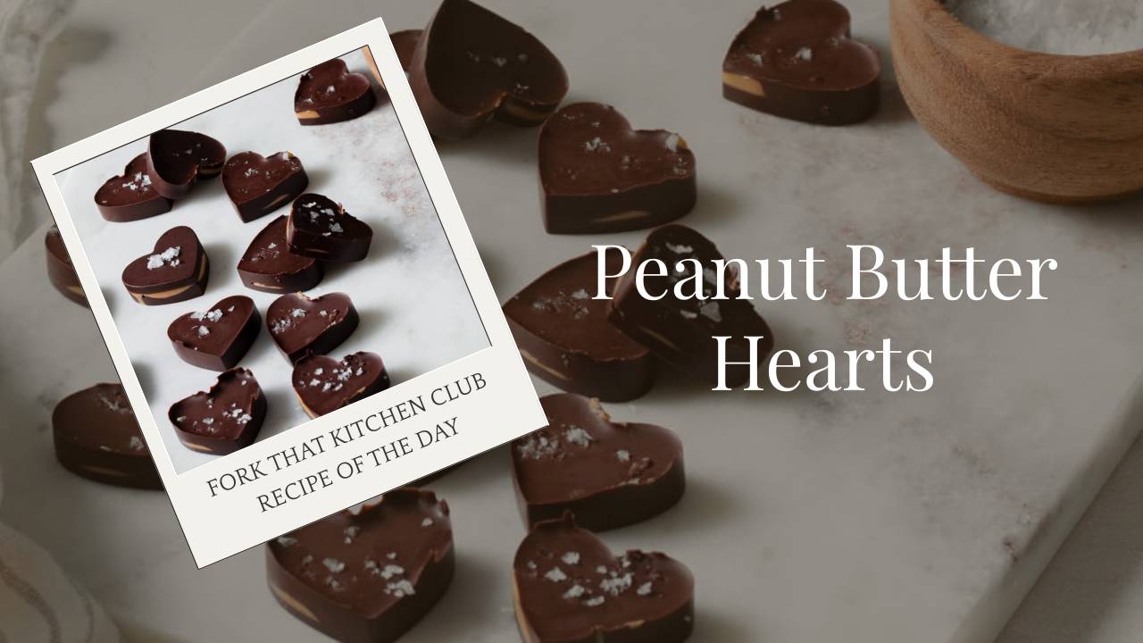 Dark chocolate peanut butter hearts arranged on a gray marble cutting board with flaky sea salt on top, small bowl of sea salt in background, and a light colored linen napkin nearby