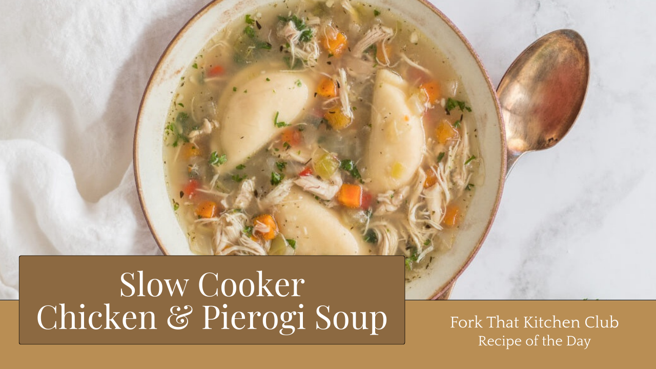 White bowl with copper rim filled with shredded chicken and vegetables in golden broth with pierogies, and fresh parsley garnish, copper spoon resting beside bowl along with a white linen napkin on the opposite side