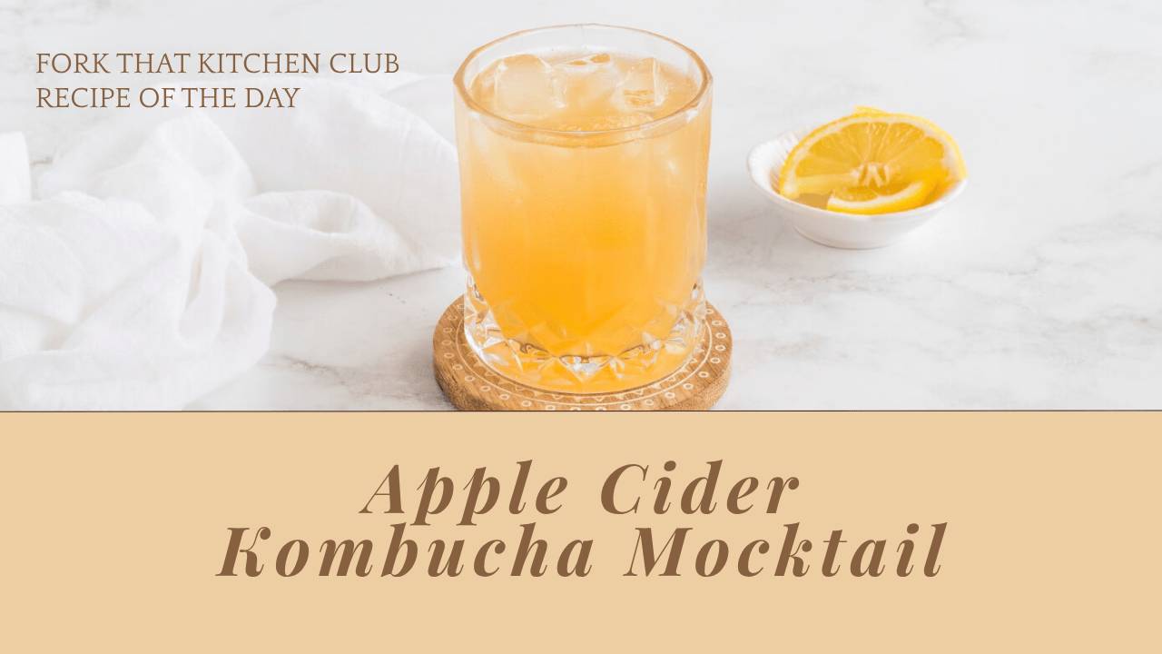 Golden apple cider kombucha mocktail served over ice in a clear glass on white marble background. 