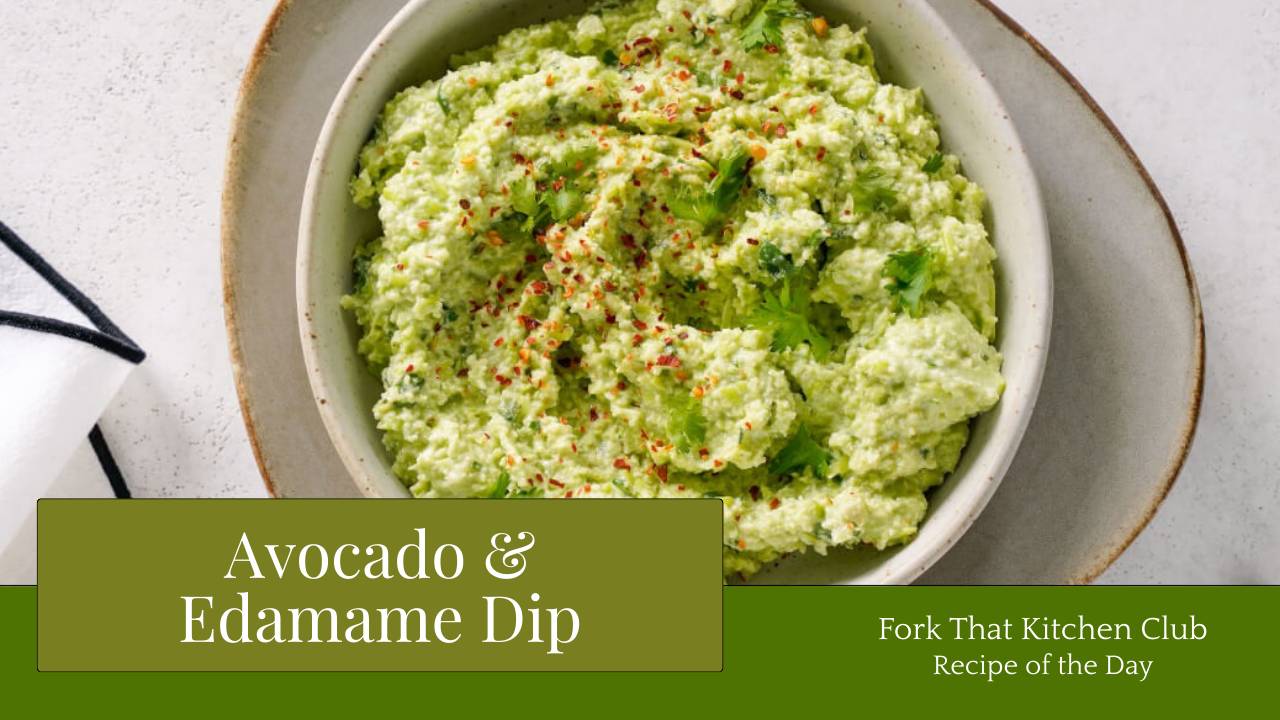 Bowl of pale green avocado and edamame dip garnished with chili flakes and cilantro, served in an off-white bowl resting on a matching plate