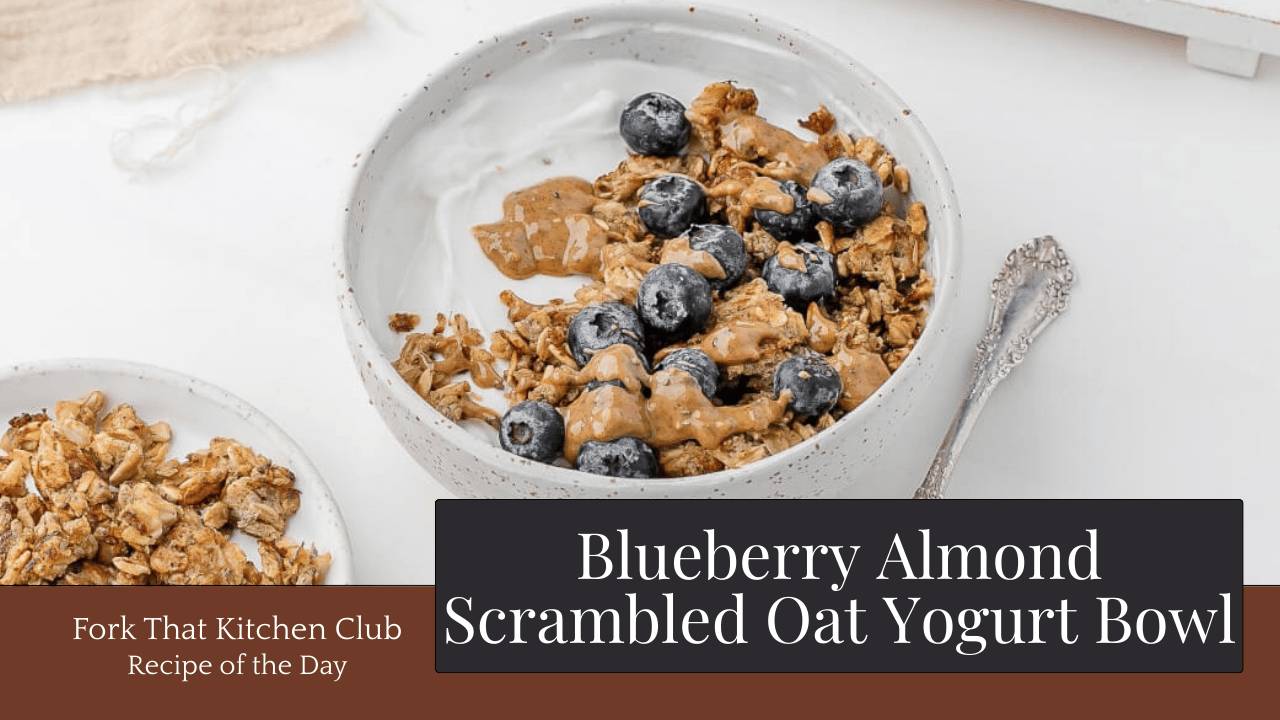 White bowl of Greek yogurt topped with golden scrambled oats, fresh blueberries, and almond butter drizzle on white table with a beige linen napkin in the background, a spoon to the rigth side, and a small white plate of additional scrambled oats on the left side