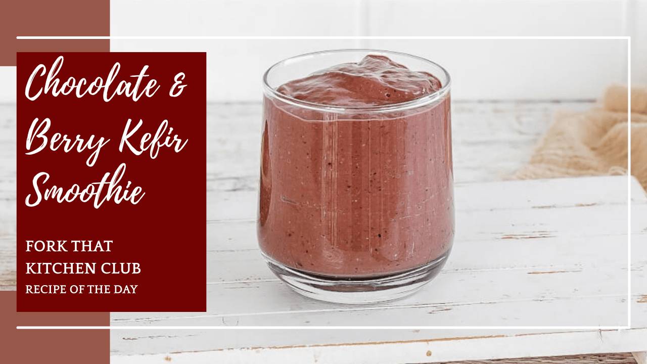 Glass of thick chocolate smoothie with visible berries and creamy texture with a beige linen napkin beside the distressed white wooden tray the glass is sitting on