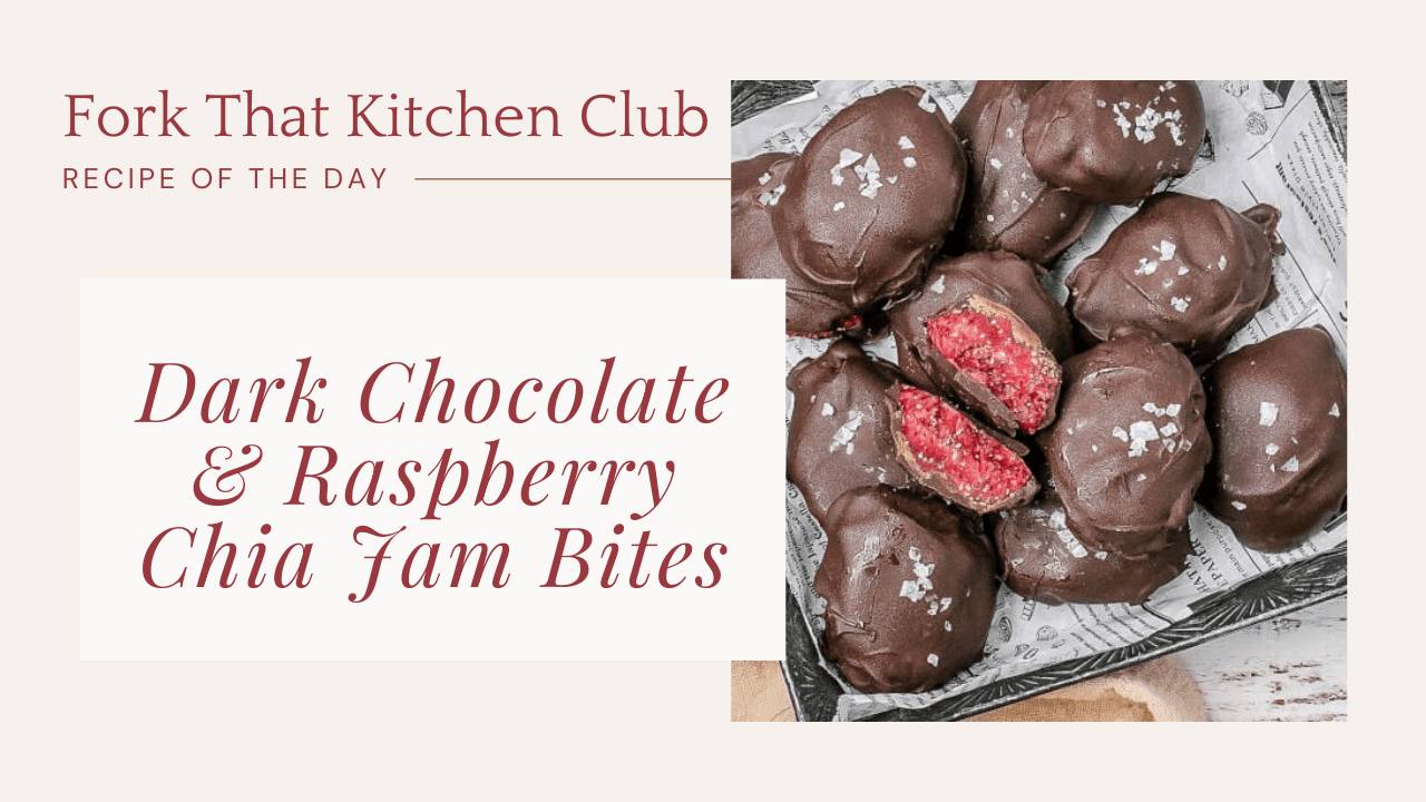 Dark chocolate covered raspberry chia jam bites on parchment-lined baking sheet with flaky sea salt sprinkled on top and one bite cut open revealing bright pink jammy center
