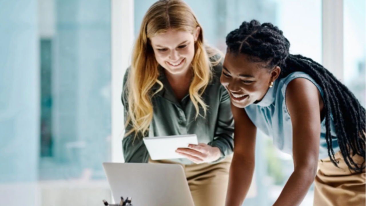 Two businesswomen collaborating at a laptop and tablet in a modern office